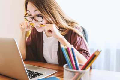woman biting pencil while sitting on chair in front of computer during daytime, word of the day, pulchritudinous